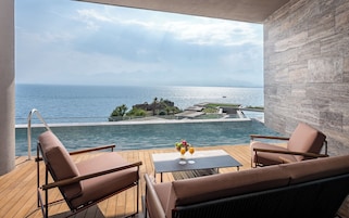 A balcony with a view of the sea, a pool, and a table with drinks.