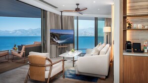A modern hotel room with a large window offering a view of the sea and mountains, a flat-screen TV, a ceiling fan, and a cozy seating area with a coffee machine. - Divan Talya (Antalya)