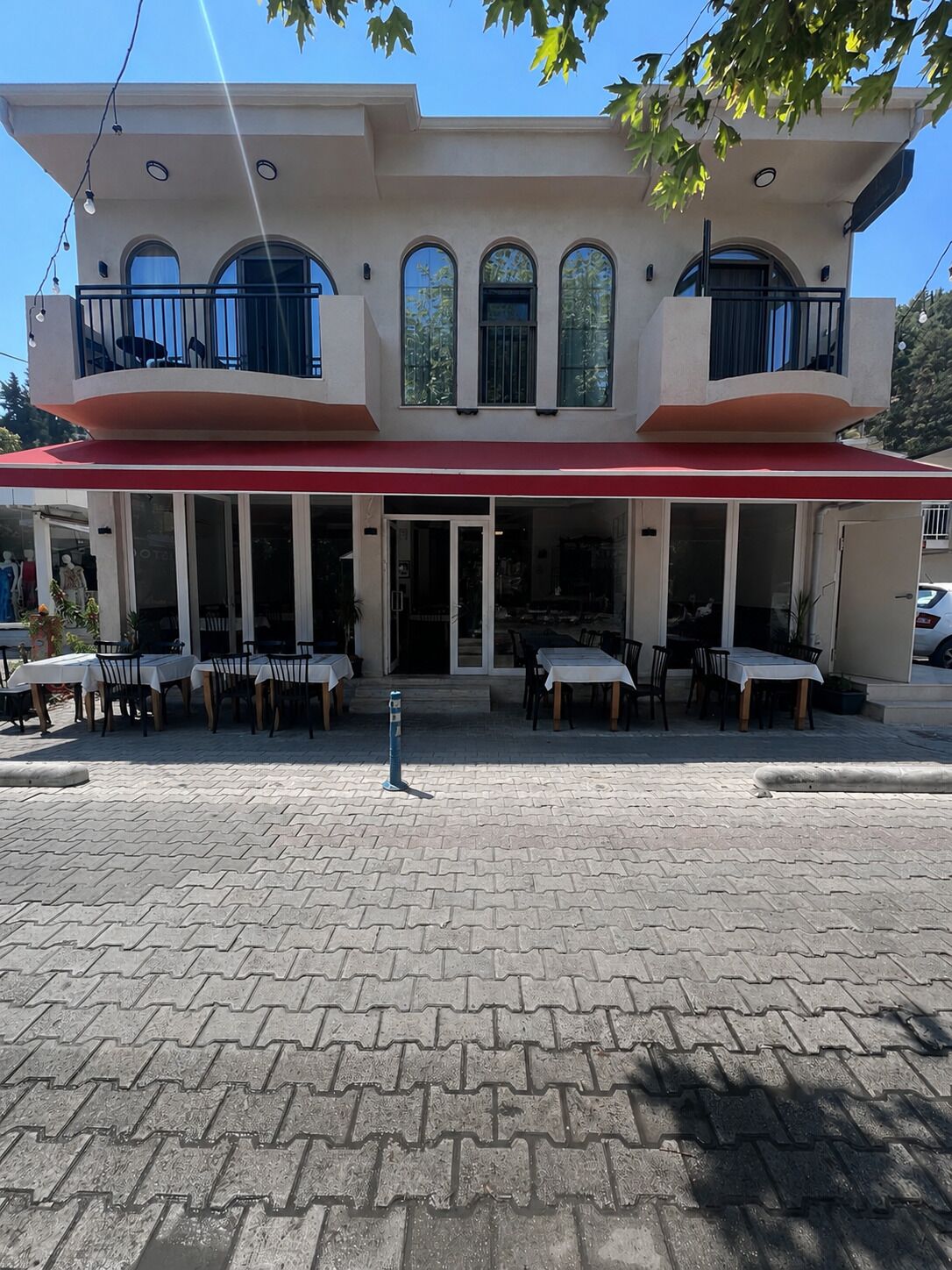 A two-story building with a red awning, multiple windows, and outdoor seating.