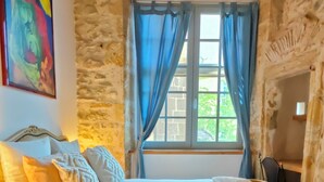 Une chambre à coucher avec un lit, une table de chevet, une lampe, une fenêtre avec des rideaux et un tableau au mur.