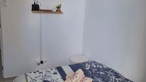 A bedroom with a bed, a mounted TV, a small shelf with decorative items, and a power outlet. - Studio in the Drôme Provençale. Suze's Cocoon. (Suze-la-Rousse)
