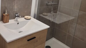 A modern bathroom with a white sink, wooden vanity, and a glass-enclosed shower area. - Studio in the Drôme Provençale. Suze's Cocoon. (Suze-la-Rousse)