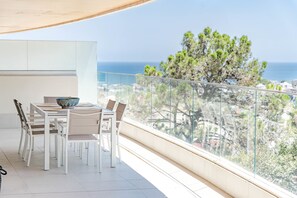 Un balcon avec une table et des chaises pour prendre les repas, une vue sur la mer et un arbre.