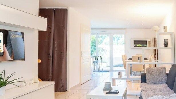 A modern living room with a sofa, coffee table, and TV. There is a dining area with chairs and a table in the background. - Maison des Pralets I T4 I Etrembières (Étrembières)