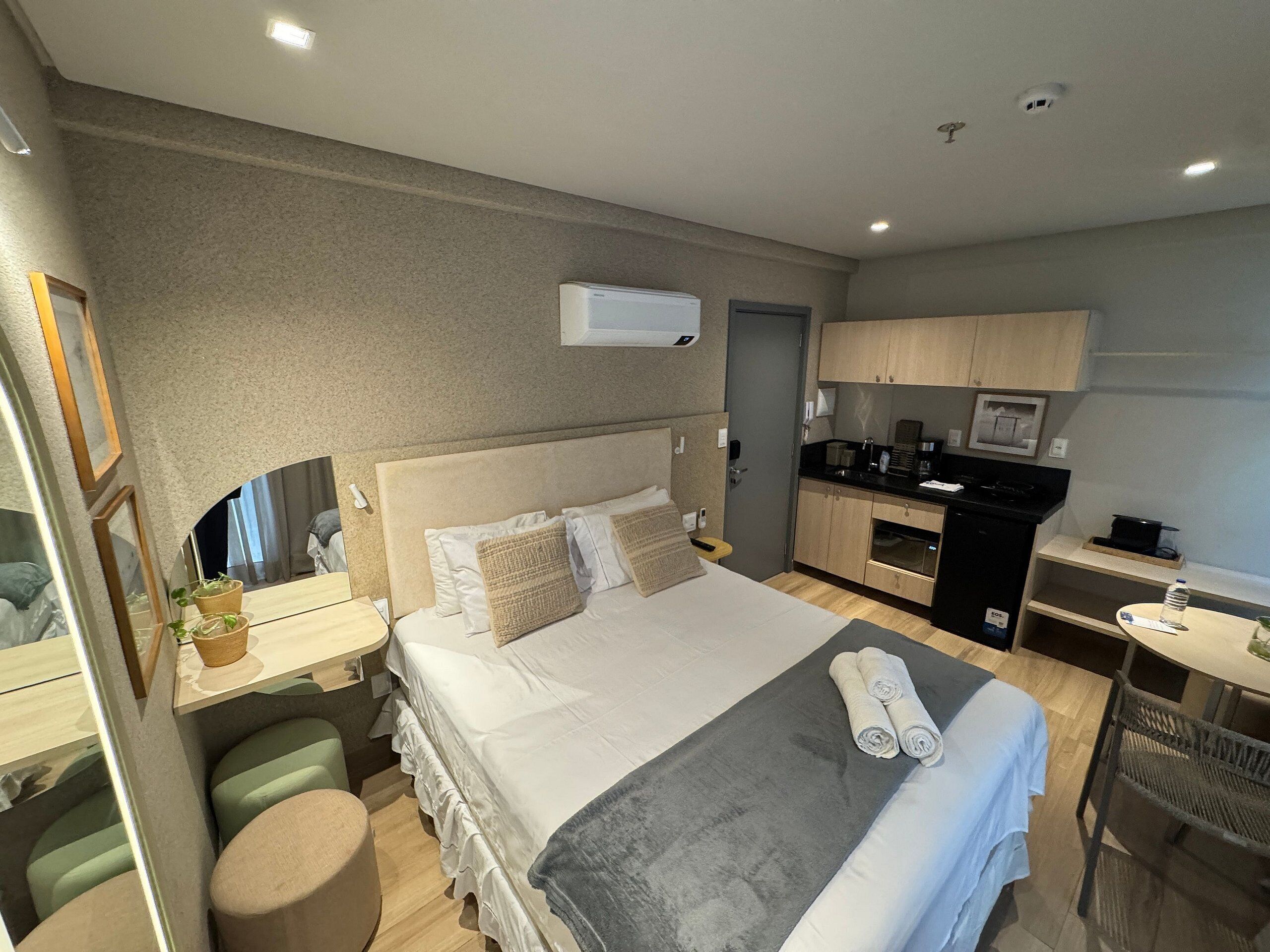 Habitación de hotel con cama, mesita de noche y una pequeña kitchenette.