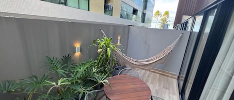A balcony with a wooden table and wicker chairs, surrounded by potted plants.