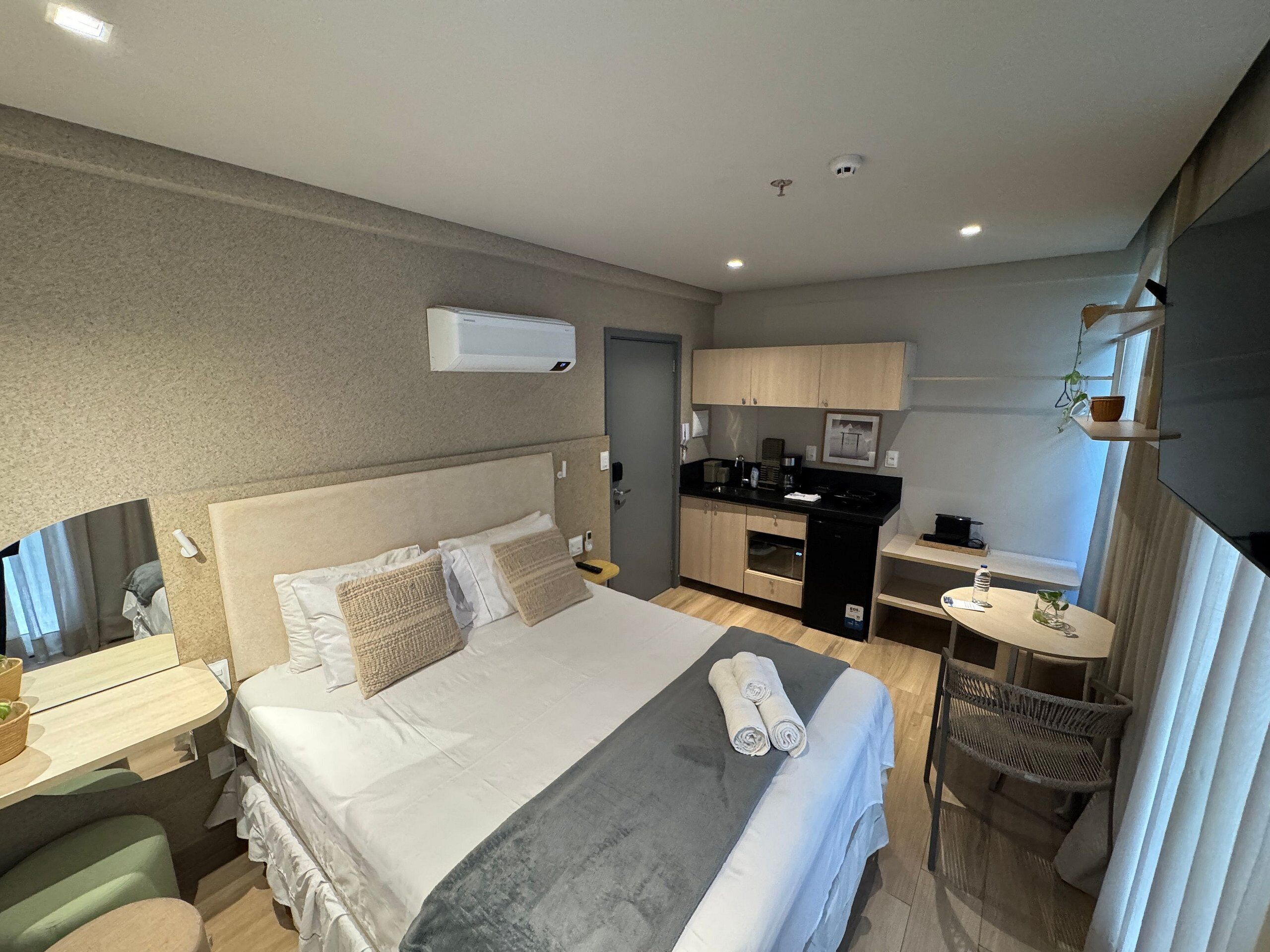 Una habitación de hotel con una cama, una kitchenette pequeña, un escritorio y una silla.