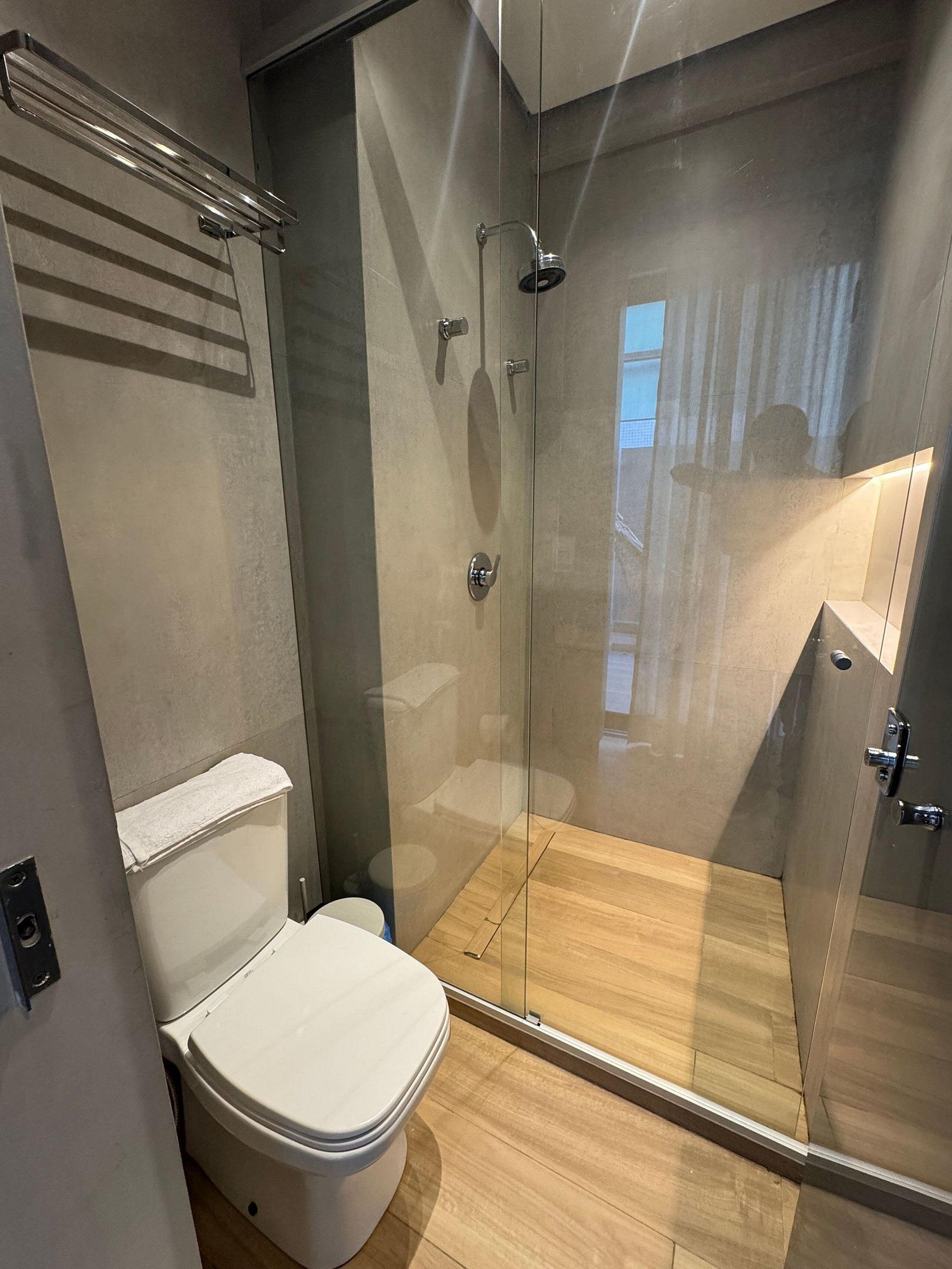Um banheiro moderno com chuveiro de vidro, vaso sanitário e porta-toalhas.