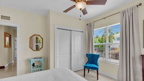A bedroom with a bed, a ceiling fan, a window with curtains, a door, and a small table with a chair. - **LA BELLA CAPRI @ CASA MARINA** Estate & Pool + Last Key White Glove Service... (Key West)
