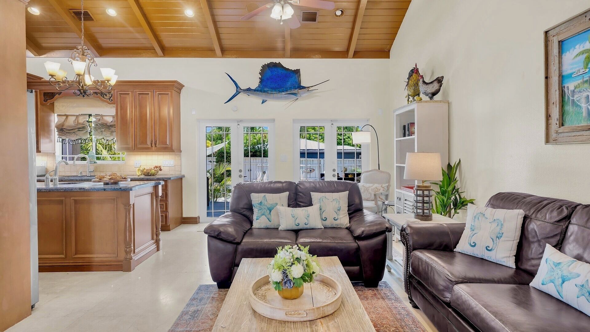 A spacious living area with a leather sofa, a coffee table with a floral centerpiece, and a ceiling fan.