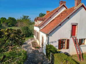Ein schmaler Steinweg führt zu einer Reihe traditioneller Gebäude mit roten Ziegeldächern und weißen Wänden.