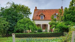 A house with a red-tiled roof, surrounded by a garden with various plants and a fence. - CHAMBERAT COUNTRY HOUSE (Chambérat)