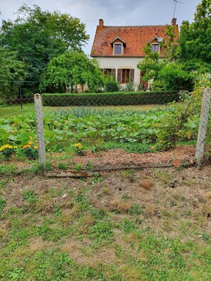 Ein Haus mit rotem Ziegeldach, umgeben von einem Garten mit verschiedenen Pflanzen und einem Zaun.