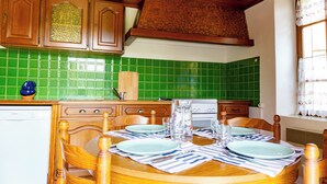A kitchen with green tiles, wooden cabinets, a dining table set with plates, glasses, and cutlery. - CHAMBERAT COUNTRY HOUSE (Chambérat)