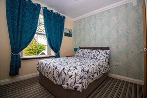 Un dormitorio con cama, cortinas, ventana y papel tapiz estampado.
