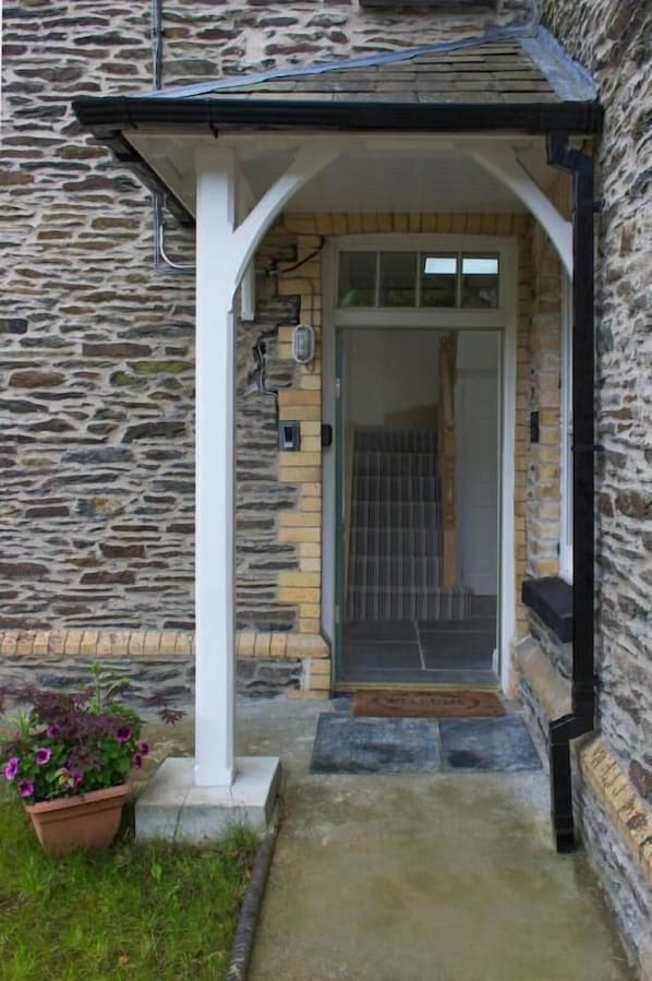 A stone building with a covered entrance, a potted plant, and a door with a metal gate.