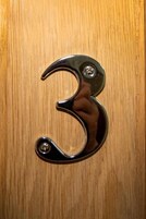 Una puerta de madera con un pomo metálico con el número 3.