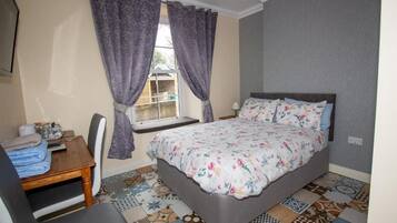 A bedroom with a bed, a desk, a chair, and a window with curtains.