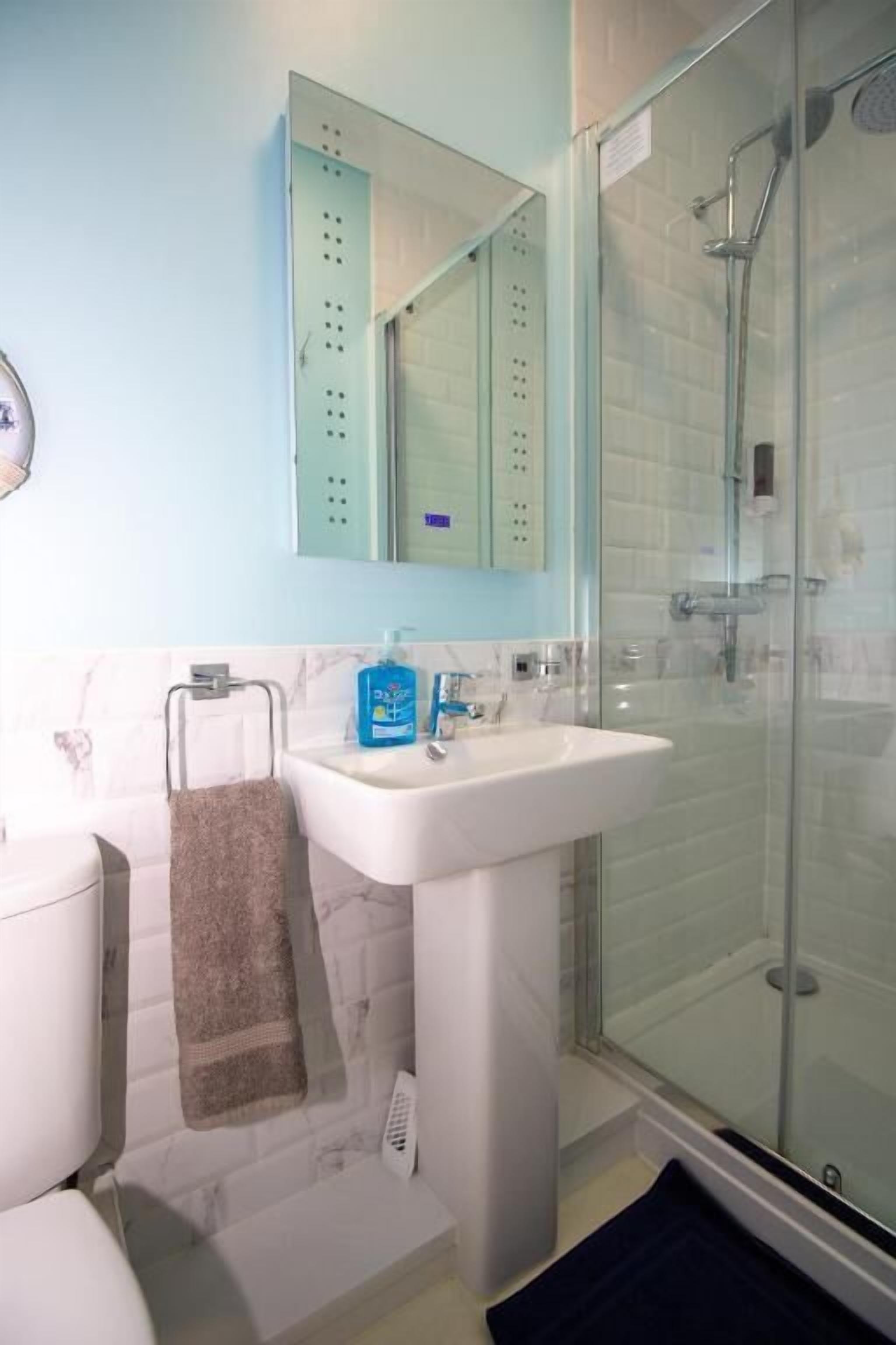 Un baño con lavamanos blanco, cabina de ducha de vidrio y perchero para toallas.