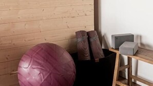 A room with a wooden slatted wall, a black storage unit with exercise equipment, and a small table with a chair.