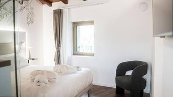 Un dormitorio con cama, una silla, un ventanal y una lámpara de pared.