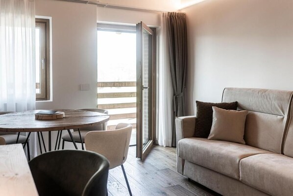 Una habitación con una mesa redonda de madera, un sofá y un ventanal corredero que da a un balcón.