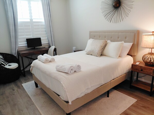 Una cama bien hecha con toallas enrolladas, una lámpara de noche, un escritorio con una computadora y una silla.