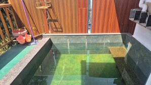 Una piscina rectangular d'aigua cristal·lina, envoltada per una tanca de fusta i un marc de pedra.