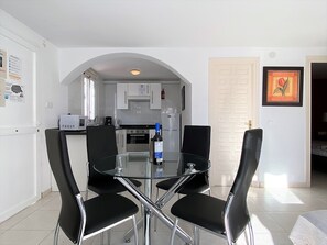 A modern kitchen with white cabinets, a microwave, and a coffee maker. There is a glass table with four black chairs. - Apartment in Nerja Near Burriana Beach (Nerja)