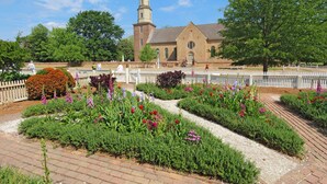 A church with a tall tower, surrounded by a garden with various flowers and a white fence.