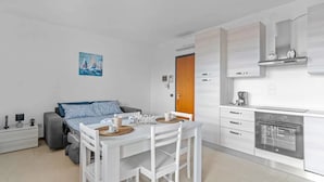 Ein modernes, kompaktes Wohnzimmer mit Bett, Esstisch und Küchenzeile.