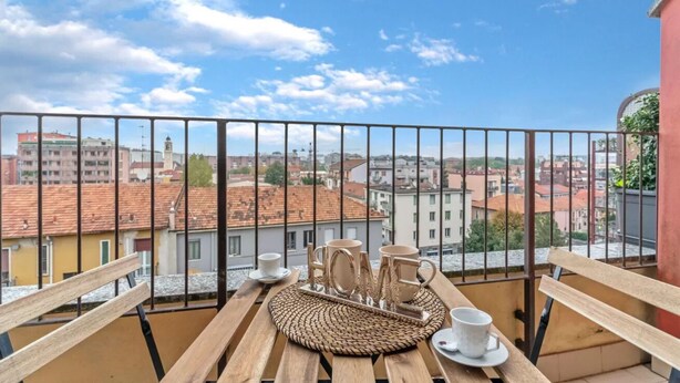 Ein Balkon mit Blick auf Gebäude, ein Holztisch mit Tassen und Untertassen sowie eine gewebte Tischmatte.