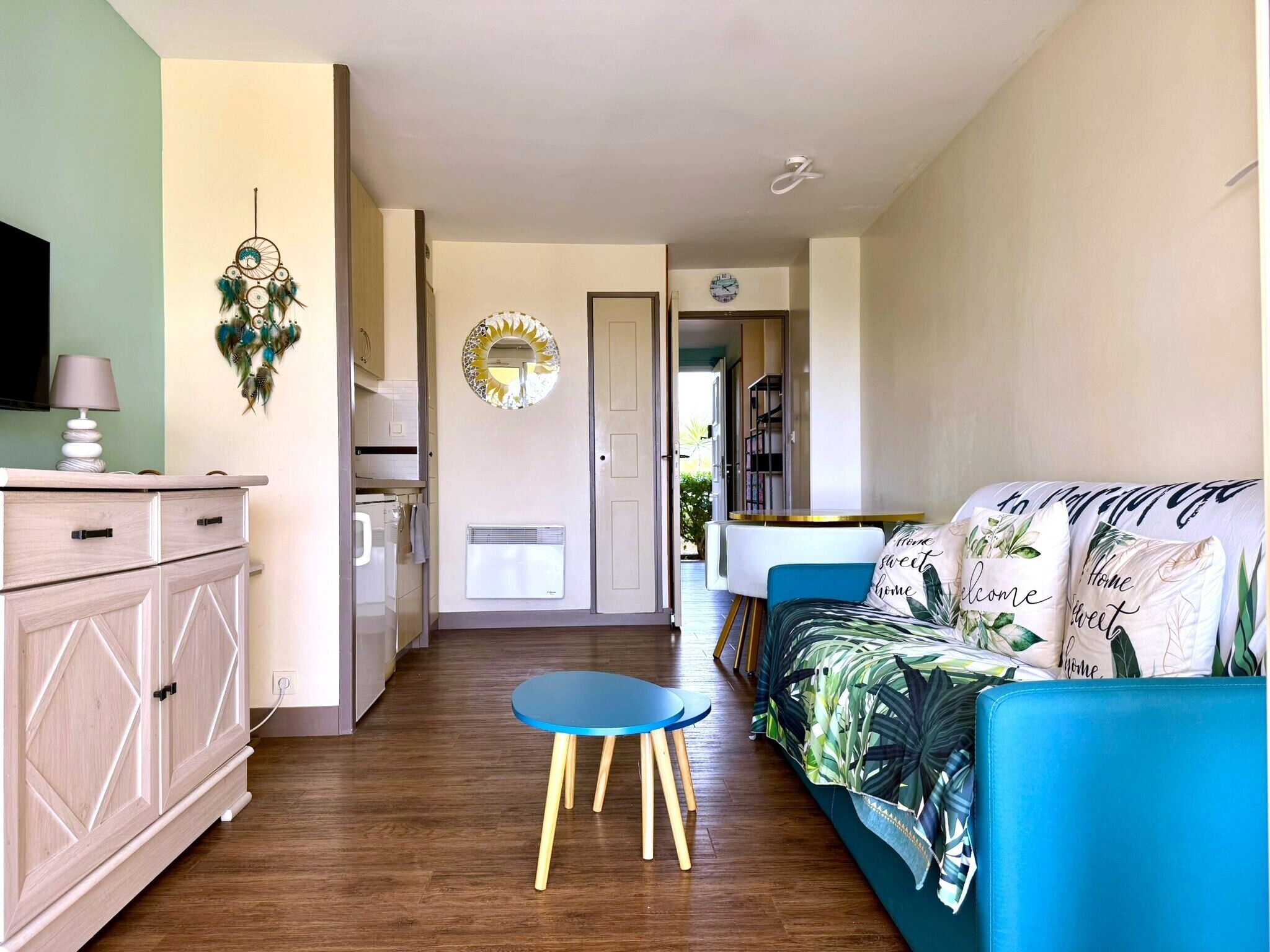 A modern living space with a kitchen, dining area, and a sofa with tropical prints.