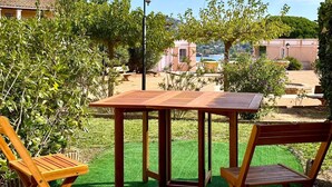 Una mesa de madera y dos sillas en un jardín con vistas a edificios y árboles.