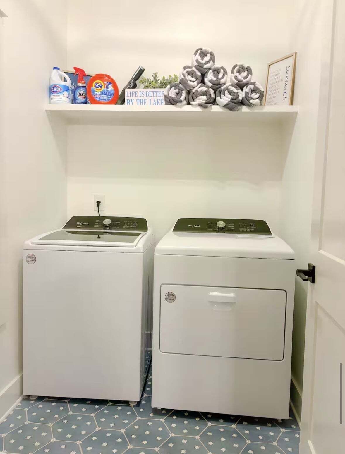 Ein Waschraum mit zwei Whirlpool Trocknern, einer Ablage für Reinigungsmittel und einem gerahmten Zitat.