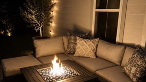 A cozy outdoor seating area with a fire feature, a cushioned sofa, and a window. - Luxury Lake Living- Pool , Fire Pit, Amenities 5 Bedroom Home (Winchester)