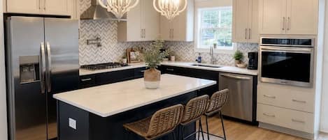 A modern kitchen with a large island, stainless steel appliances, and pendant lighting.