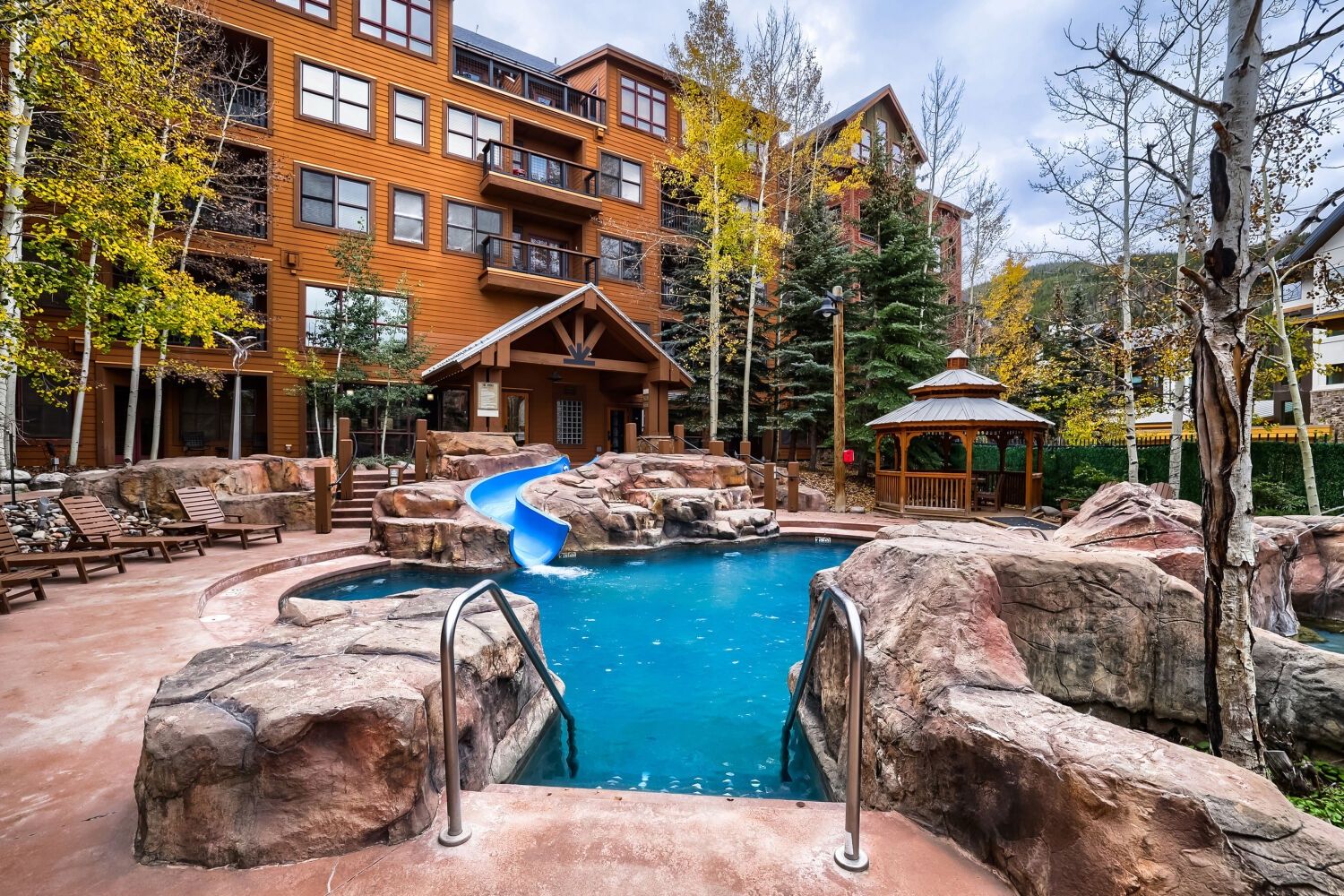 A pool area with a water slide, lounge chairs, and a building with multiple balconies.