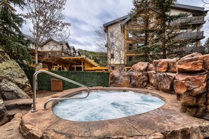 A hot tub surrounded by natural rock formations and a building with balconies. - 8836 The Springs 1 Bedroom Condo (Keystone)