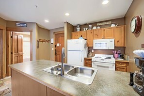 Une cuisine avec des meubles en bois, un évier en acier inoxydable, un réfrigérateur blanc, un four à micro-ondes et une cuisinière.