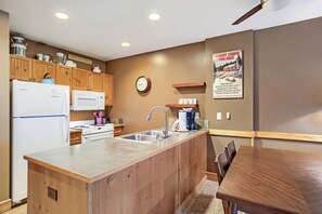 A kitchen with wooden cabinets, a refrigerator, a microwave, a sink, and a clock on the wall. - 8836 The Springs 1 Bedroom Condo (Keystone)