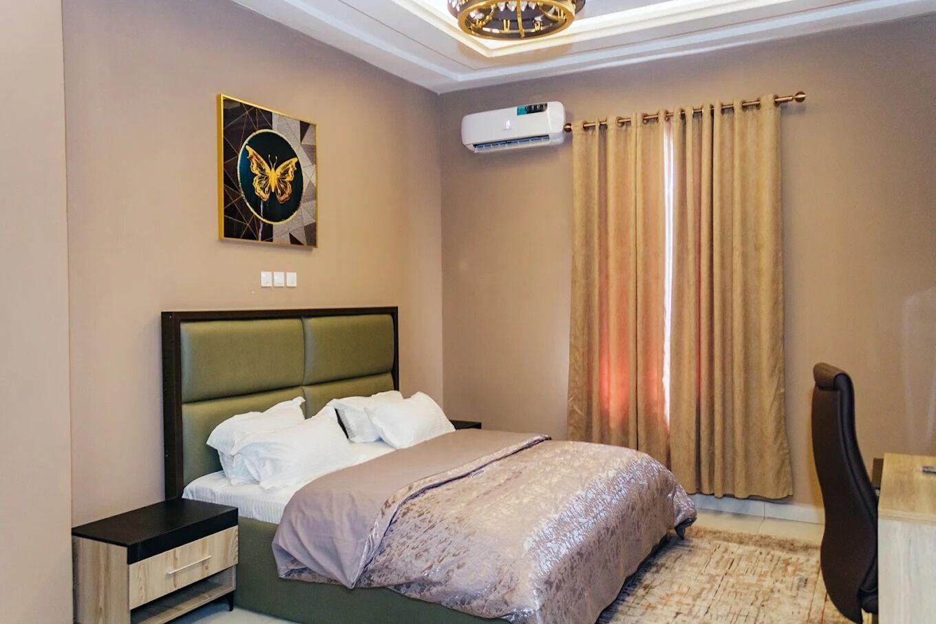 Una camera d'albergo con un letto, una scrivania, un condizionatore d'aria, una tenda e un'opera d'arte appesa al muro.
