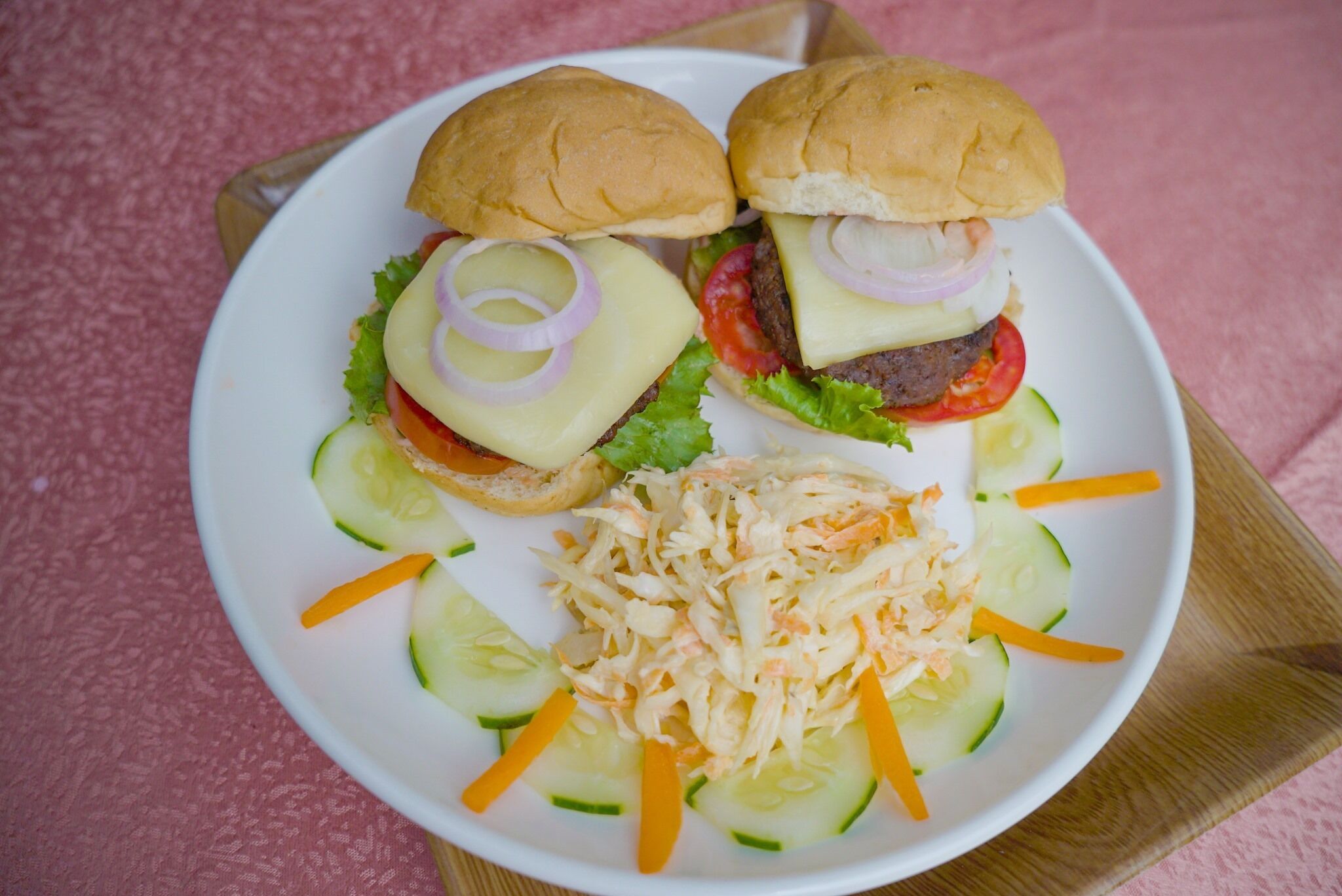 Ein Teller mit zwei Burgern, Salat, Tomate, Zwiebeln, Käse, dazu Krautsalat und Gurkenscheiben.