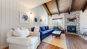 Ein Wohnzimmer mit Sofa, Sessel, Kamin und gerahmten Kunstwerken an der Wand.