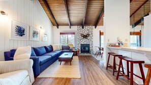 A living room with a blue sofa, a fireplace, wooden flooring, and a stone wall. - Discovery 4 #132 2 Bedroom Condo (Mammoth Lakes)