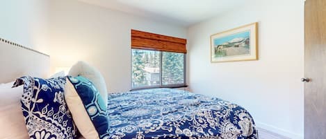 A bedroom with a large bed, a window with a view, a framed picture on the wall, and a door.