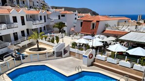 Una piscina con diseño en forma de corazón, rodeada por un edificio blanco con balcones y vista al mar.