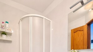 Un baño moderno con cabina de ducha, inodoro, tocador con espejo y una pequeña repisa con artículos de aseo.