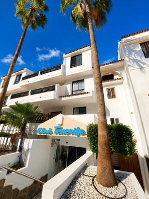 Um hotel com vários andares, varandas, palmeiras e um céu azul límpido.