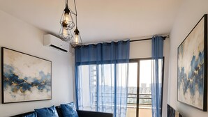 Una sala de estar moderna con un sofá negro, cojines azules, una mesa de centro redonda con flores, un televisor sobre un mueble bajo y obras de arte en las paredes.
